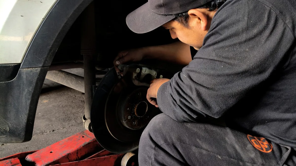 Mecánico de Automotora Sucre trabajando en el disco de freno y el tren delantero de un auto sobre el gato.